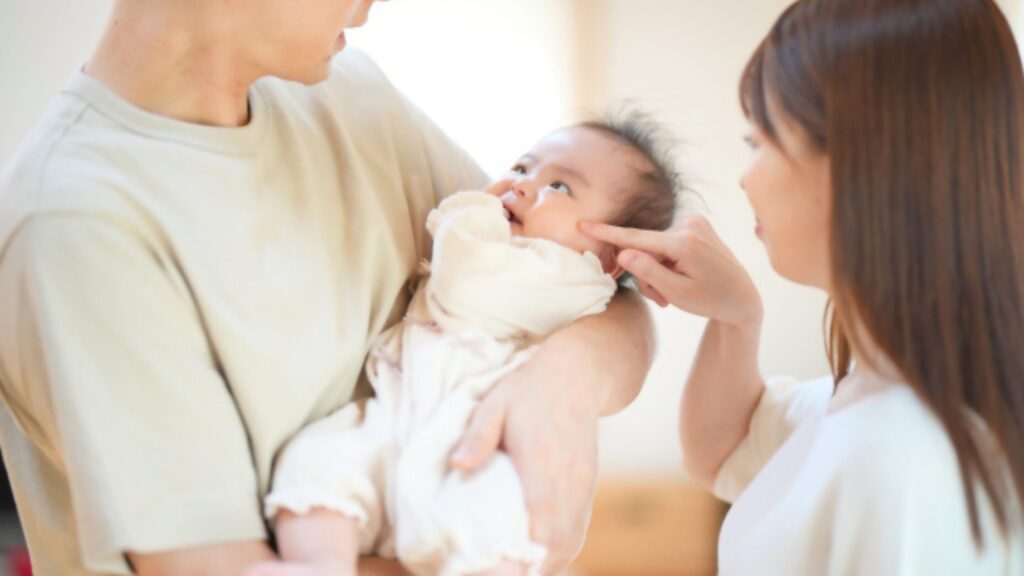 赤ちゃんを抱く父親と、それを見ている母親